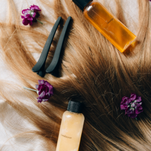 Bottles of shampoo and conditioner nestled on flowing blonde hair, accompanied by purple flowers and black hair clips—perfect for expert hair color maintenance and hair growth. 