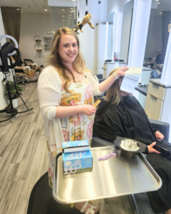 A hairdresser holds a piece of foil while preparing to color a client's hair in a modern salon, with tools and products on a metal tray nearby. - Salon Jaylee | The Villages, FL