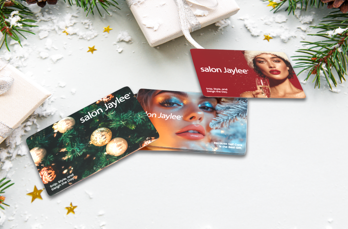 A stack of Salon Jaylee gift cards featuring a woman in festive attire on a snowy holiday-themed surface with greenery and wrapped gifts. - Salon Jaylee | The Villages, FL